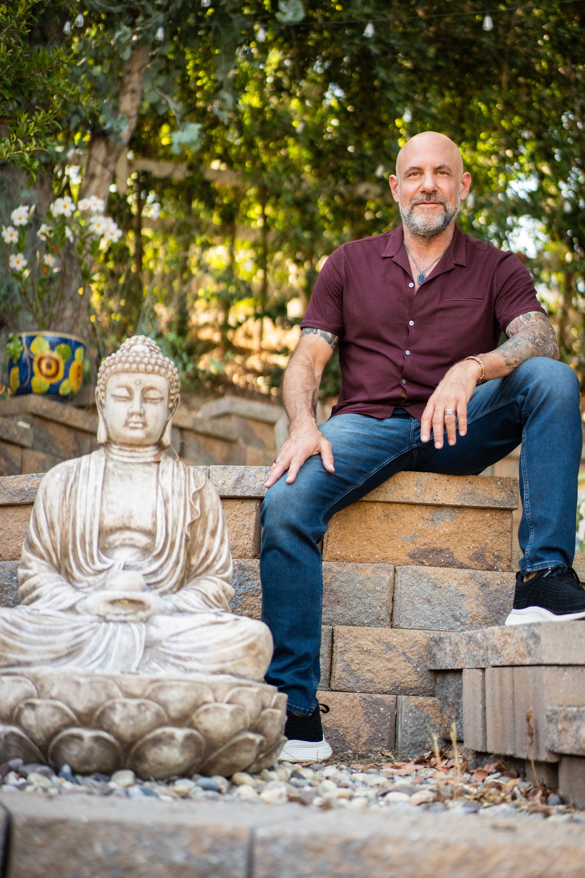Bentley Richards seated in a garden beside a Buddha statue